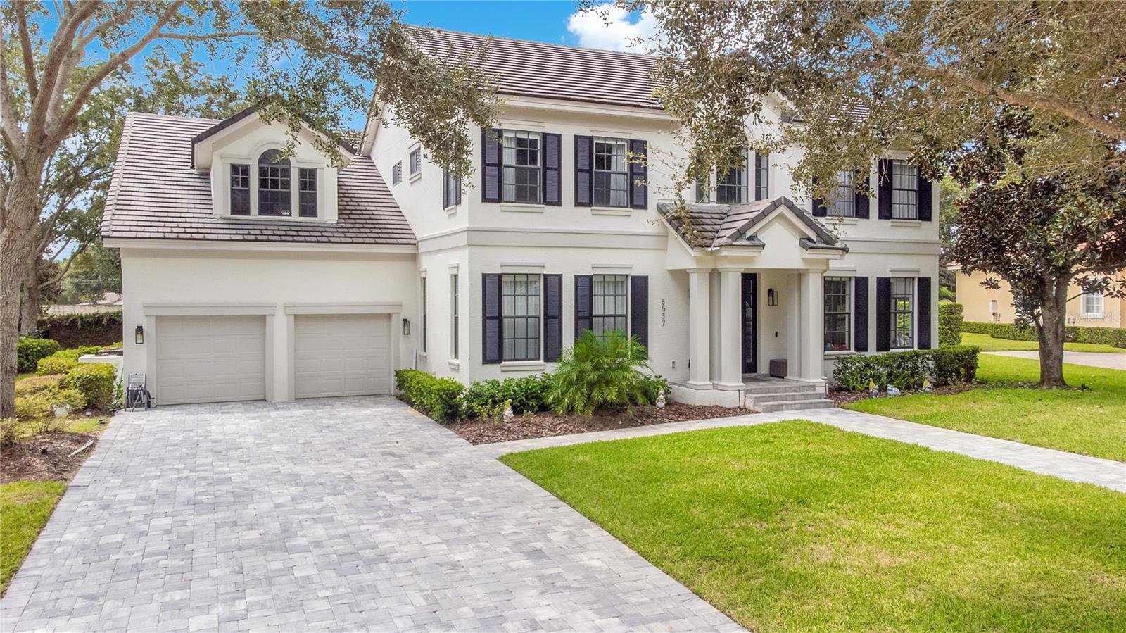 front of two story luxury home with white paint and brick driveway